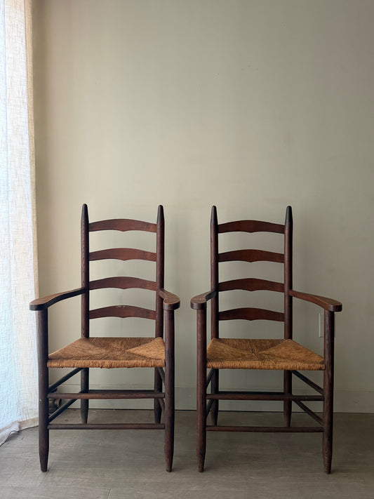 Oak ladder back rush seat dining chairs with arms. Sold as a pair.