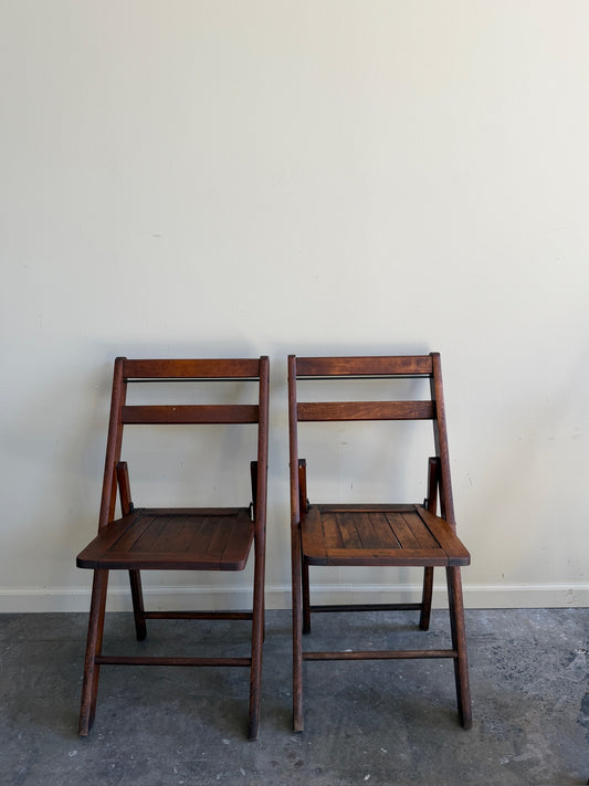 Stained pine folding chairs. Sold as a pair.